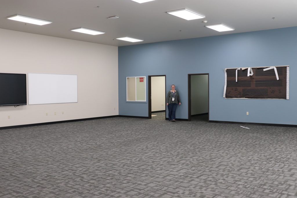 Large empty room with blue wall and a blond woman with curly hair smiling