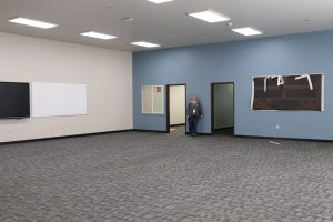 Large empty room with blue wall and a blond woman with curly hair smiling