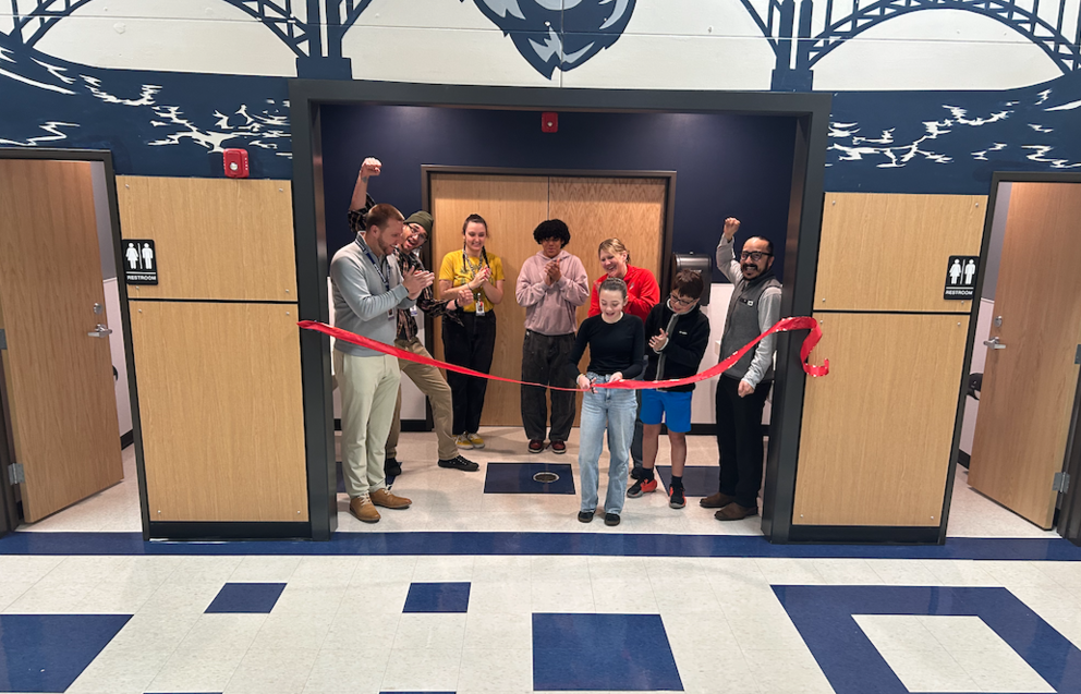Young female student cutting a red ribbon in front of finished bathrooms at NMS