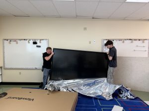Two men lifting a big screen in a classroom