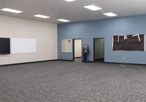 Large empty room with blue wall and a blond woman with curly hair smiling