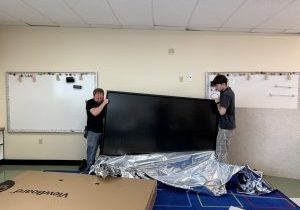 Two men lifting a big screen in a classroom